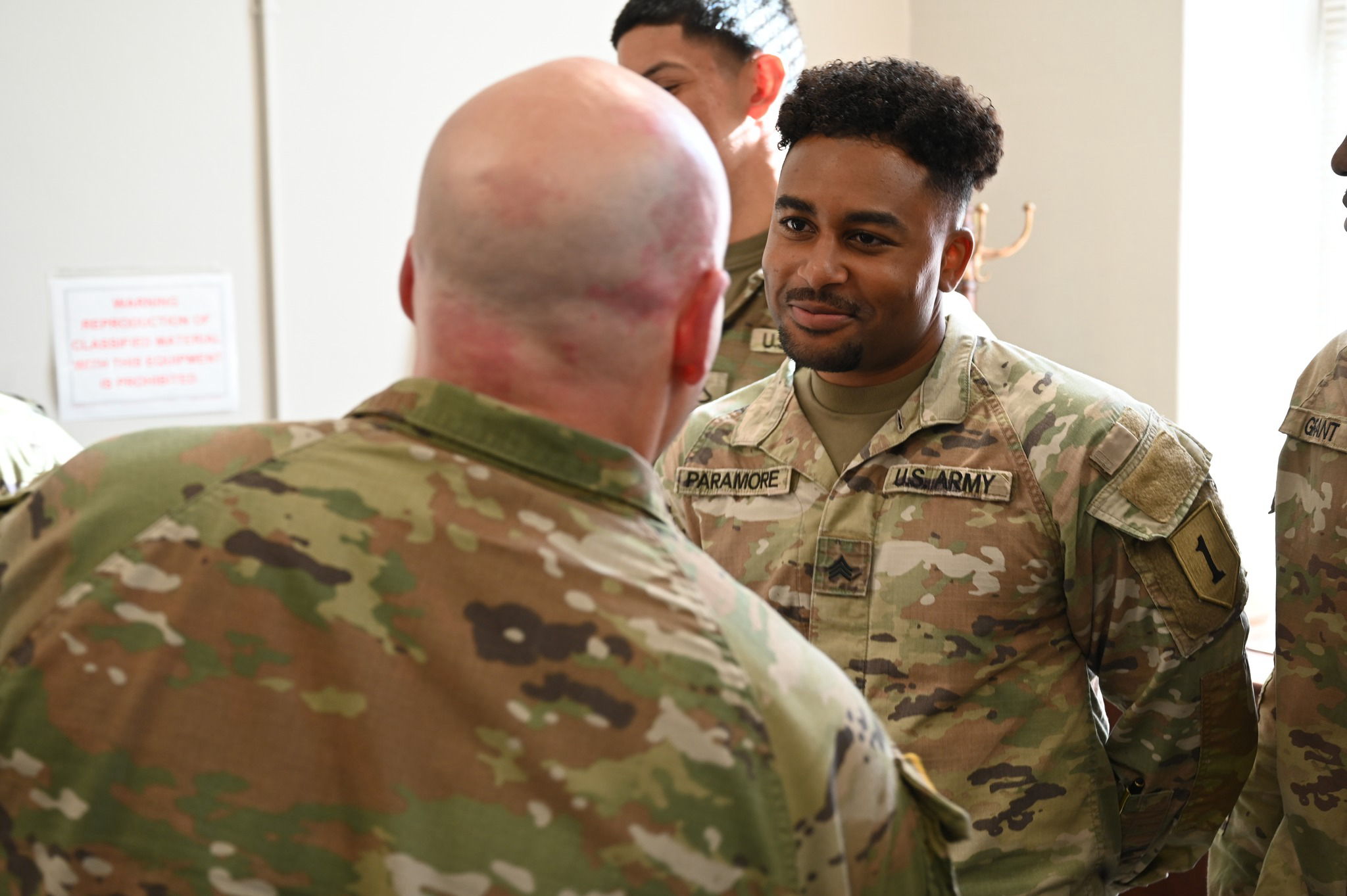 Two military personnel in camouflage engage in conversation, showcasing camaraderie and teamwork in a professional setting.