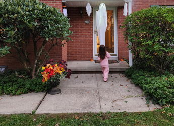 A charming suburban home with a child in pink, festive decorations, green shutters, and colorful flowers evokes joy and warmth.