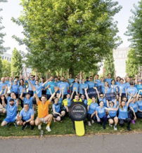 A joyful group in matching blue shirts celebrates outdoors, embodying unity and teamwork, with Garmin banners in a vibrant setting.