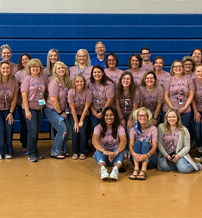 A joyful team in matching pink t-shirts smiles together in a gym, expressing camaraderie and a sense of community.