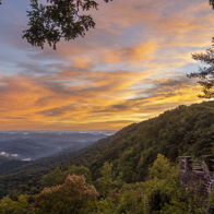 Mountainous landscape at sunset with vibrant skies, lush greenery, and a viewpoint overlooking a serene valley.