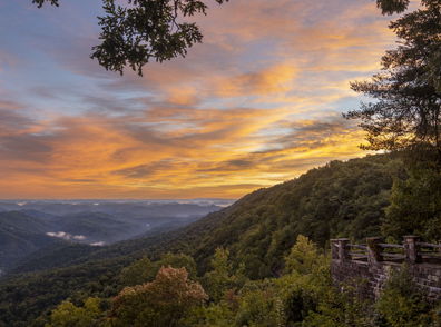 Mountainous landscape at sunset with vibrant skies, lush greenery, and a viewpoint overlooking a serene valley.