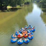 Group of people on inner tubes in a calm river, enjoying a sunny day among greenery, evoking joy and relaxation.