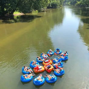 Group of people on inner tubes in a calm river, enjoying a sunny day among greenery, evoking joy and relaxation.