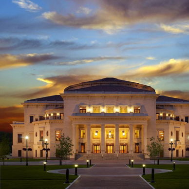 Grand theater with classical design at sunset, highlighted by warm colors and elegant surroundings, evoking grandeur and inspiration.