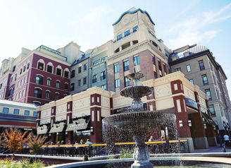 Charming building blends historical and modern styles with a fountain, vibrant colors, and inviting atmosphere under a blue sky.
