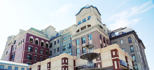 Charming building blends historical and modern styles with a fountain, vibrant colors, and inviting atmosphere under a blue sky.